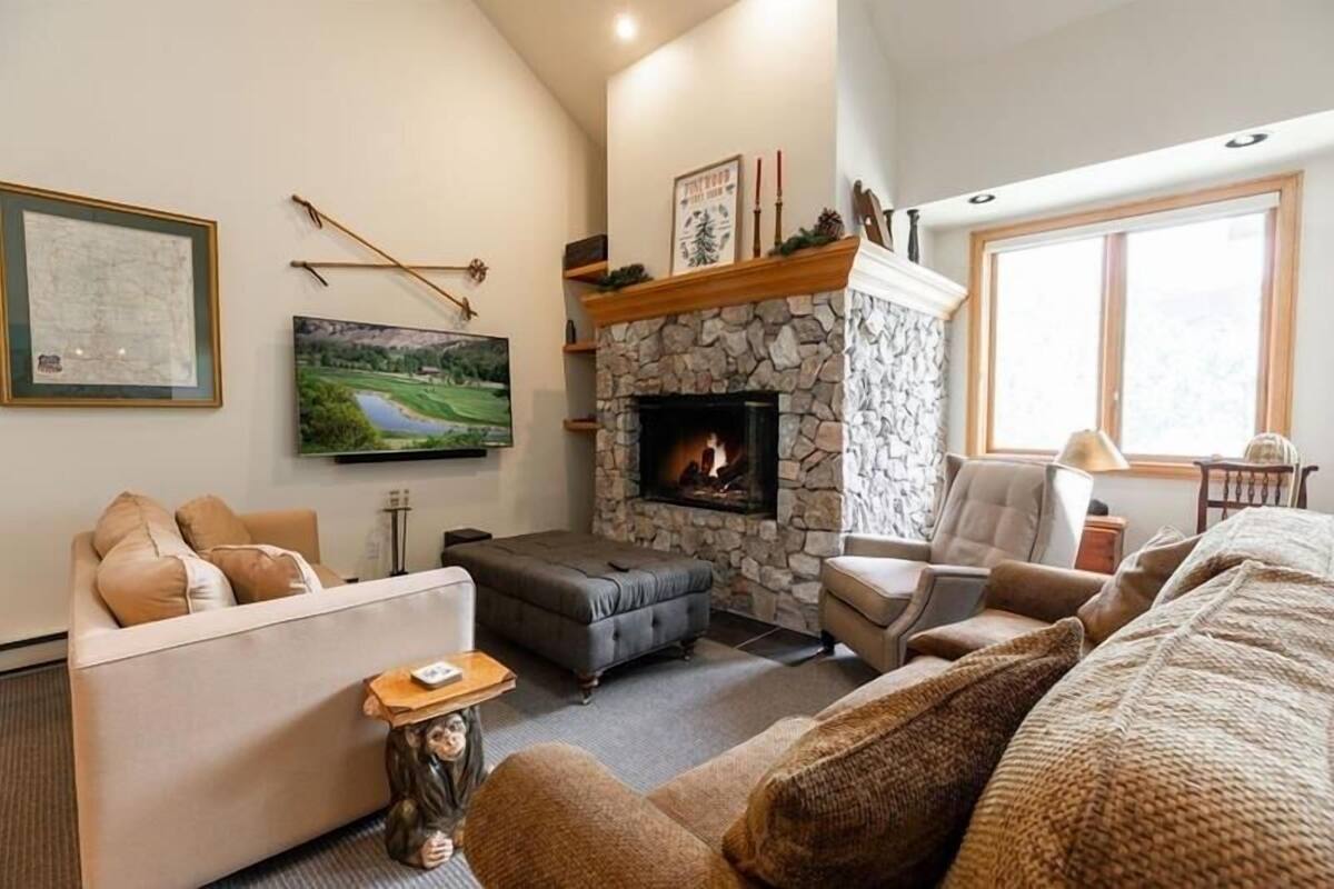 A cozy living room with a stone fireplace, a large flat-screen TV, and comfortable seating.