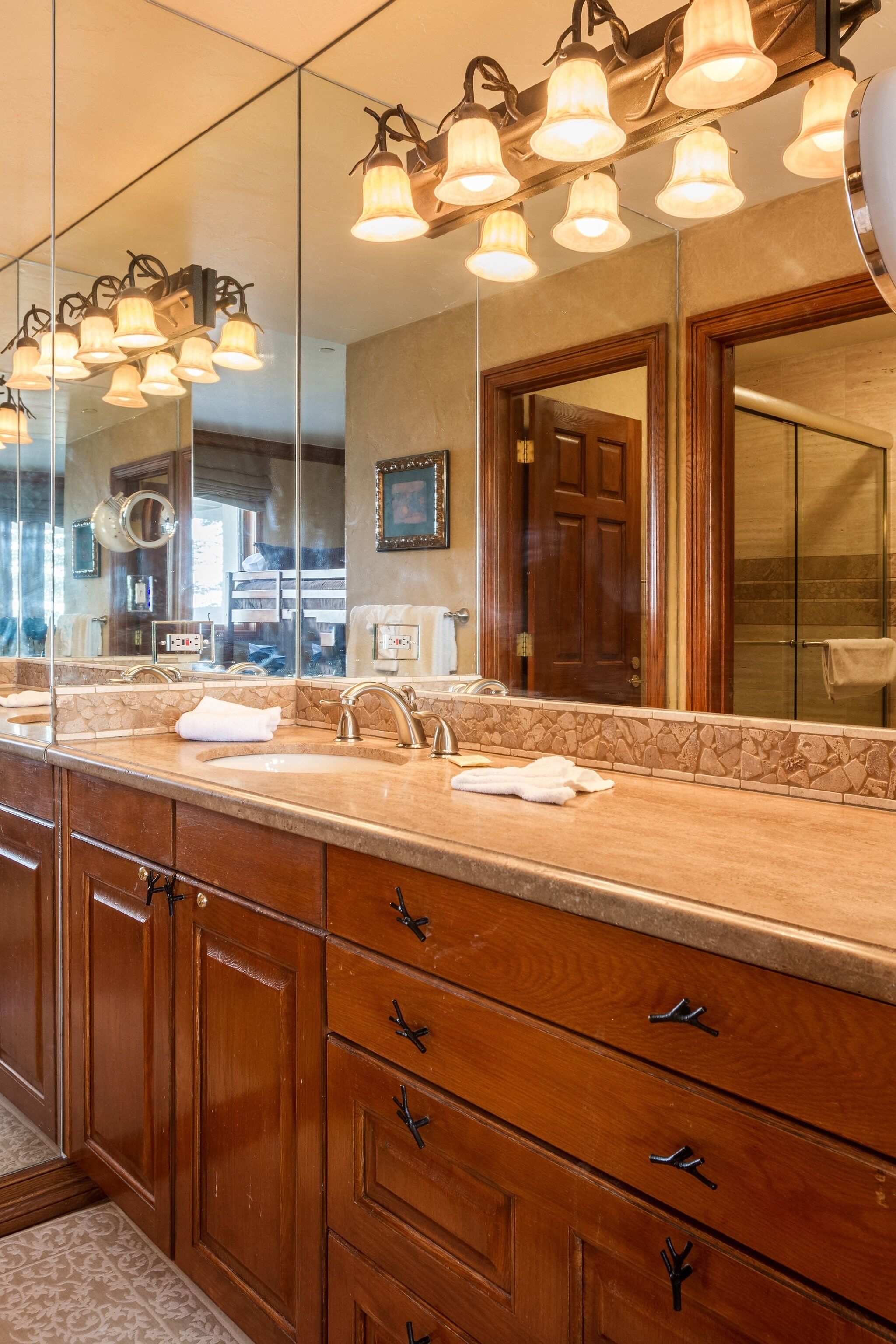 A bathroom with a large mirror, multiple light fixtures, a sink, and wooden cabinets.