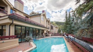 A swimming pool with a wooden deck, a building with large windows, and a view of trees and hills. - Beaver Creek Resort CO - Townsend Place & Strawberry Park Condos (Avon)