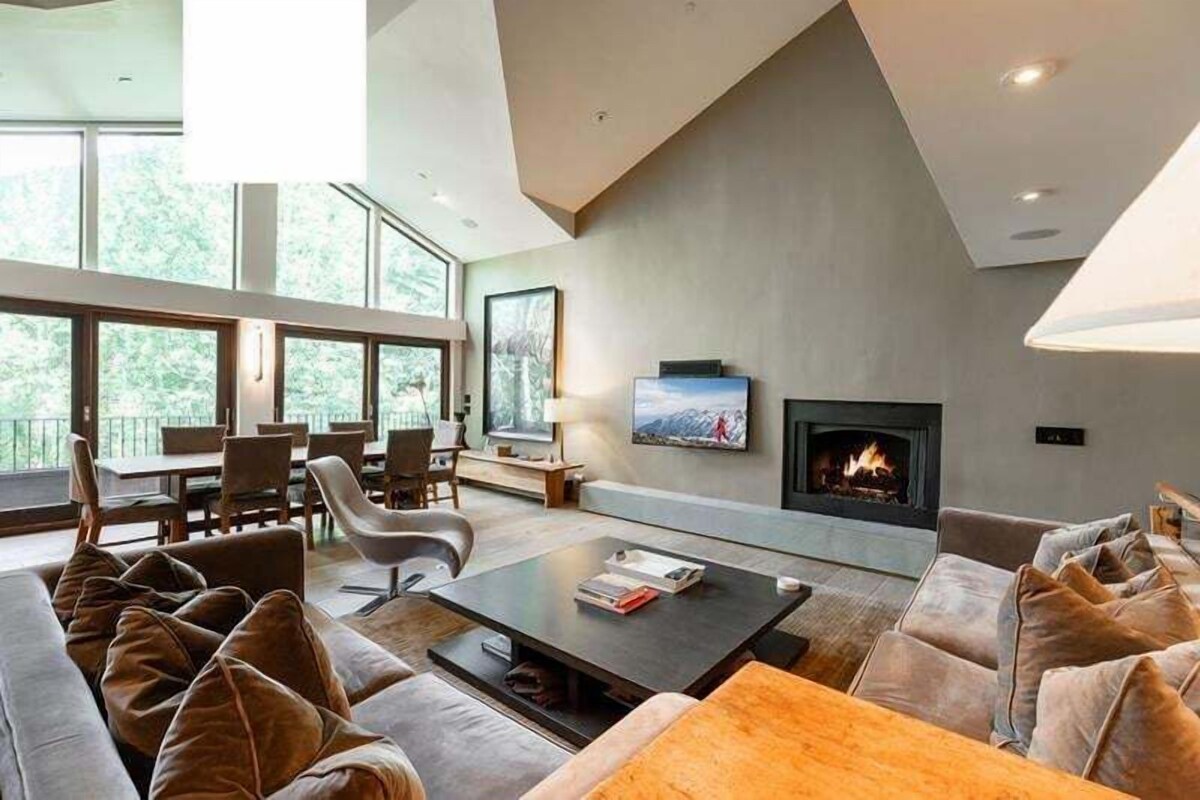 A modern living room with a fireplace, large windows, and a dining area.