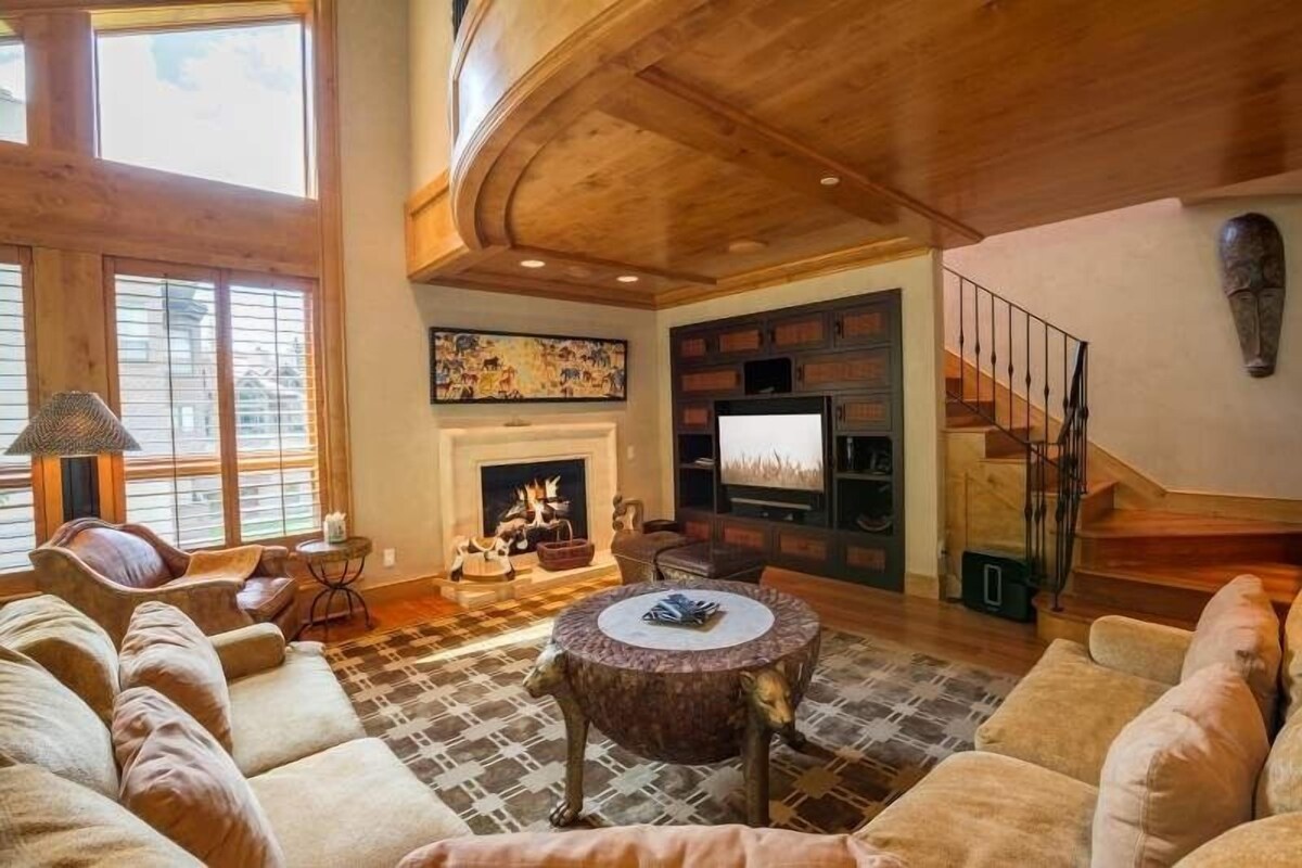 A spacious living room with a fireplace, a large window, and a staircase.