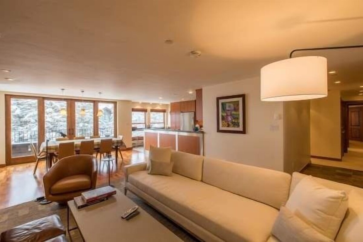 A modern living room with a sofa, coffee table, and a dining area with chairs and a table.