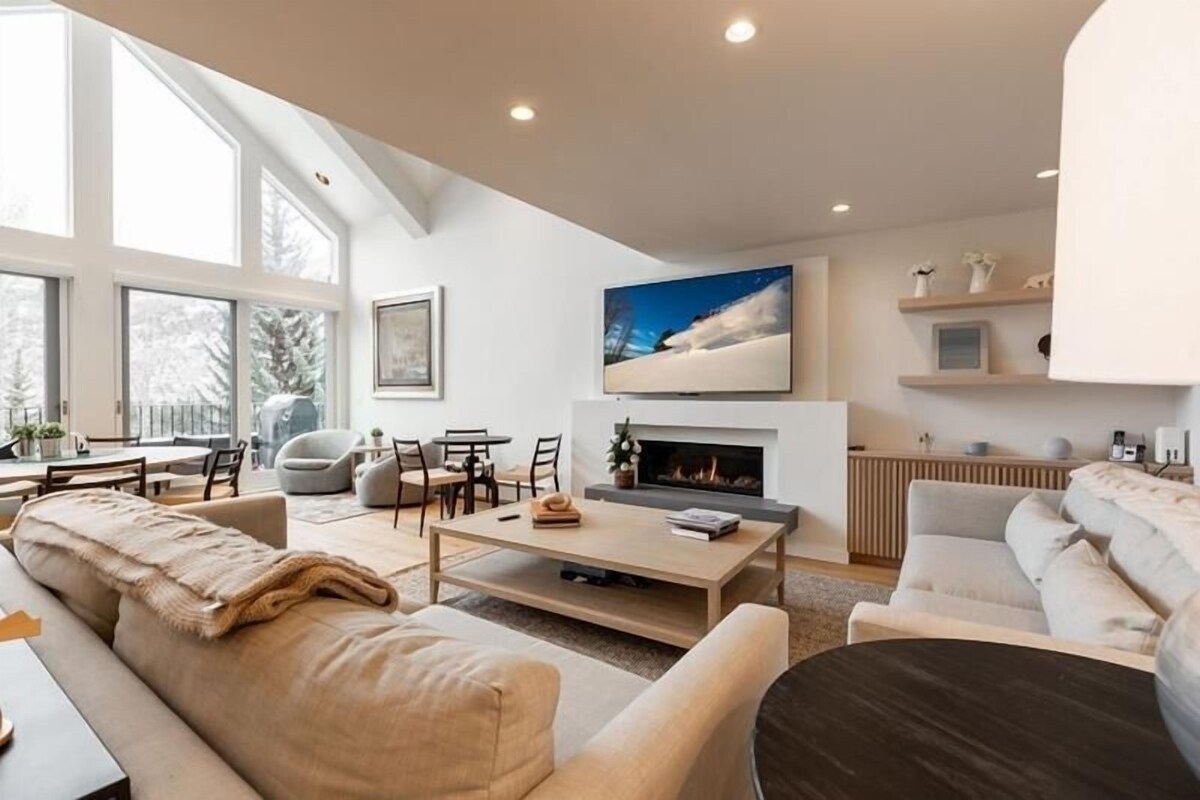 A modern living room with a fireplace, large windows, and a cozy seating area.