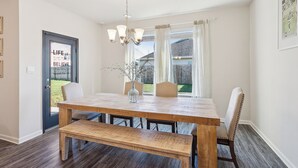 Un comedor con una mesa de madera, banco y sillas, una araña, y vista al exterior por la ventana.