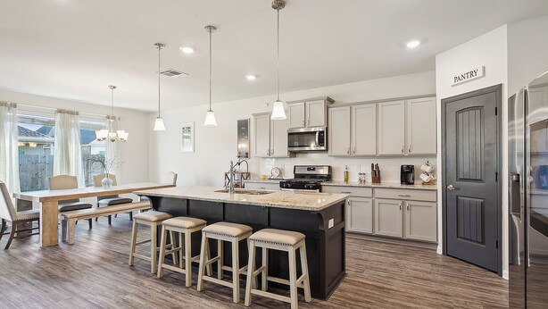 Una cocina moderna con una isla central, taburetes de bar, electrodomésticos de acero inoxidable y la puerta de una despensa.
