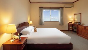 Una camera d'albergo con un letto grande, lampade sui comodini, una scrivania con il telefono, una sedia, un comò e una finestra con tende.