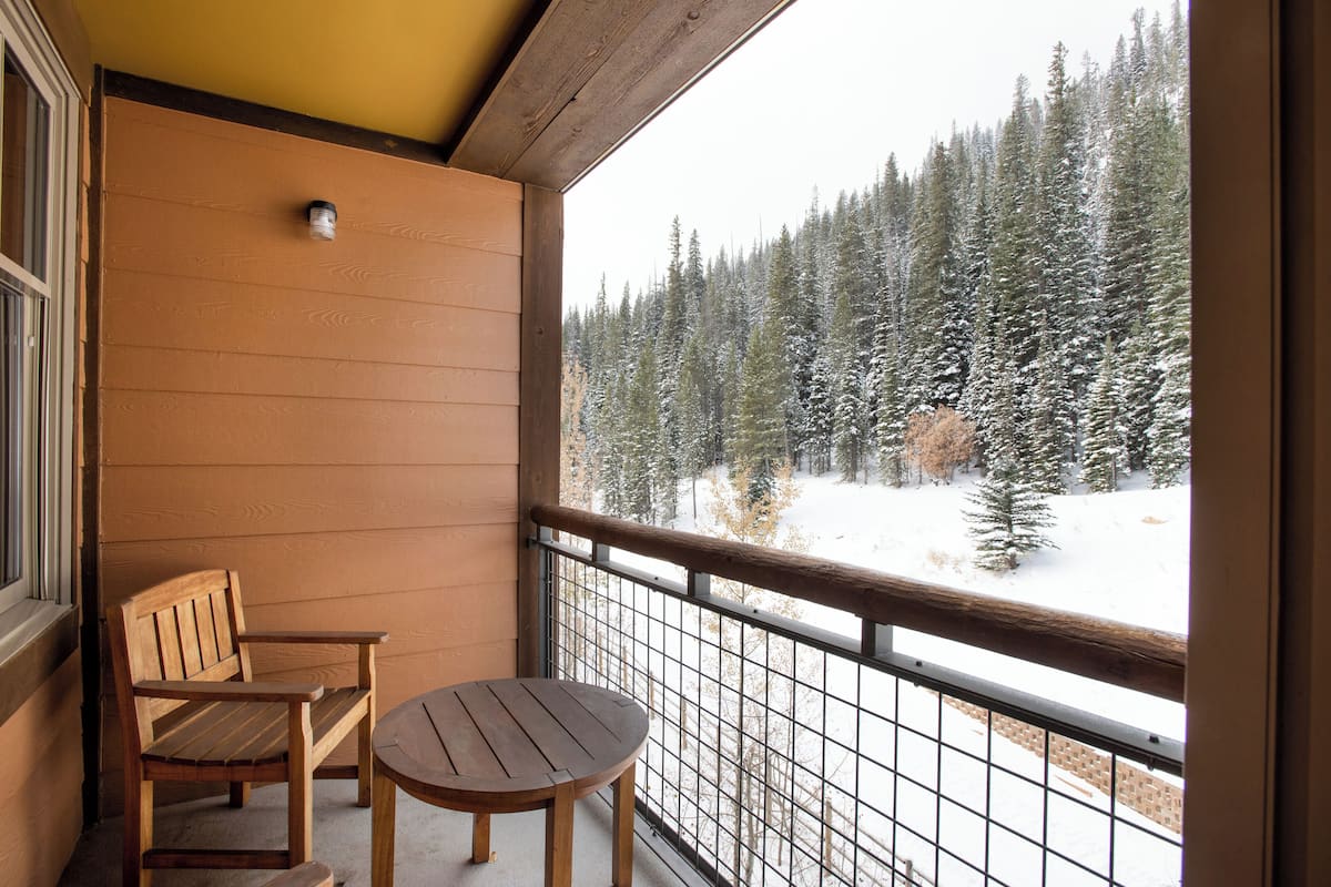 Un balcón con banco y mesa de madera, con vistas a un bosque nevado.