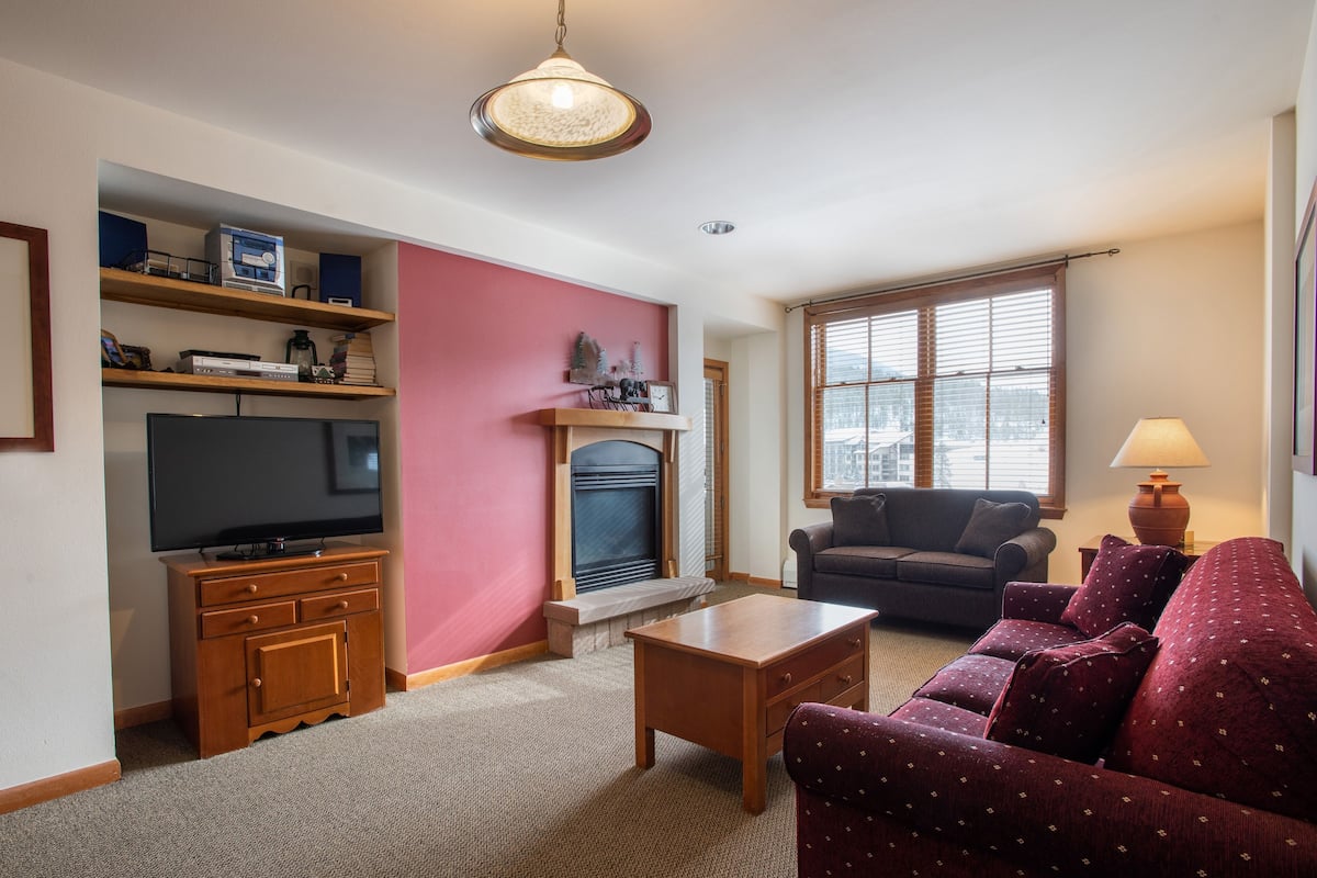 Una sala de estar con televisión, chimenea, sofá y mesa de centro.