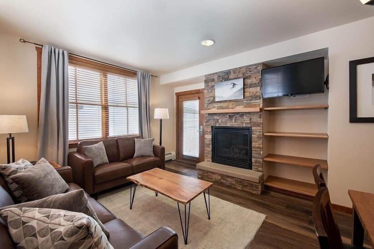 A living room with a fireplace, a sofa, a coffee table, and a TV mounted on the wall.