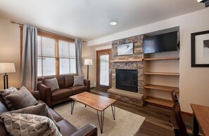 A living room with a fireplace, a sofa, a coffee table, and a TV mounted on the wall. - Zephyr Mountain Lodge Condos (Winter Park)