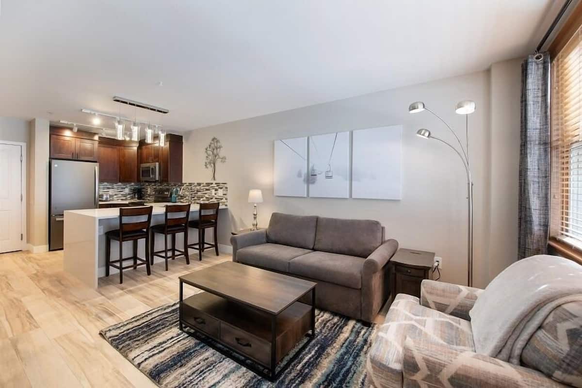 A modern living room with a sofa, coffee table, and a kitchen area with a bar.