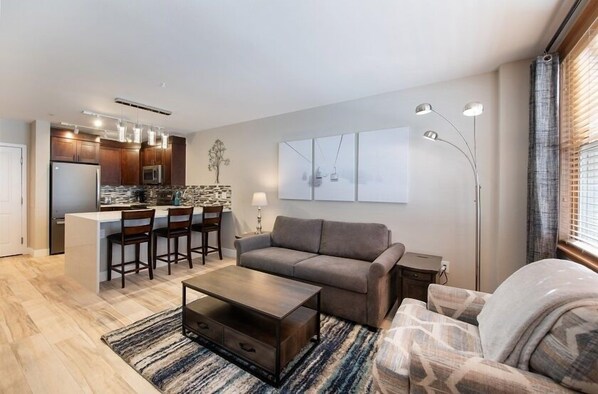 A modern living room with a sofa, coffee table, and a kitchen area with a bar. - Zephyr Mountain Lodge Condos (Winter Park)