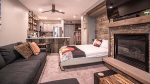 Ein modernes Wohnzimmer mit einer Couch, einem Bett, einem Kamin und einer Küche im Hintergrund.