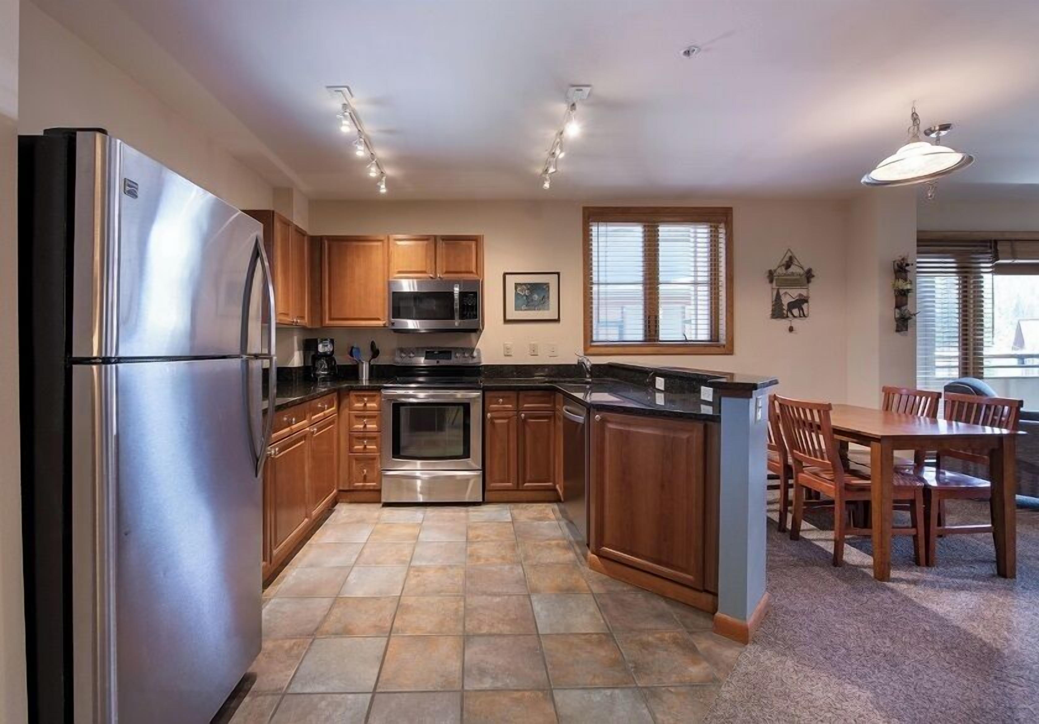 A modern kitchen with stainless steel appliances, wooden cabinets, and a dining area with a table and chairs.