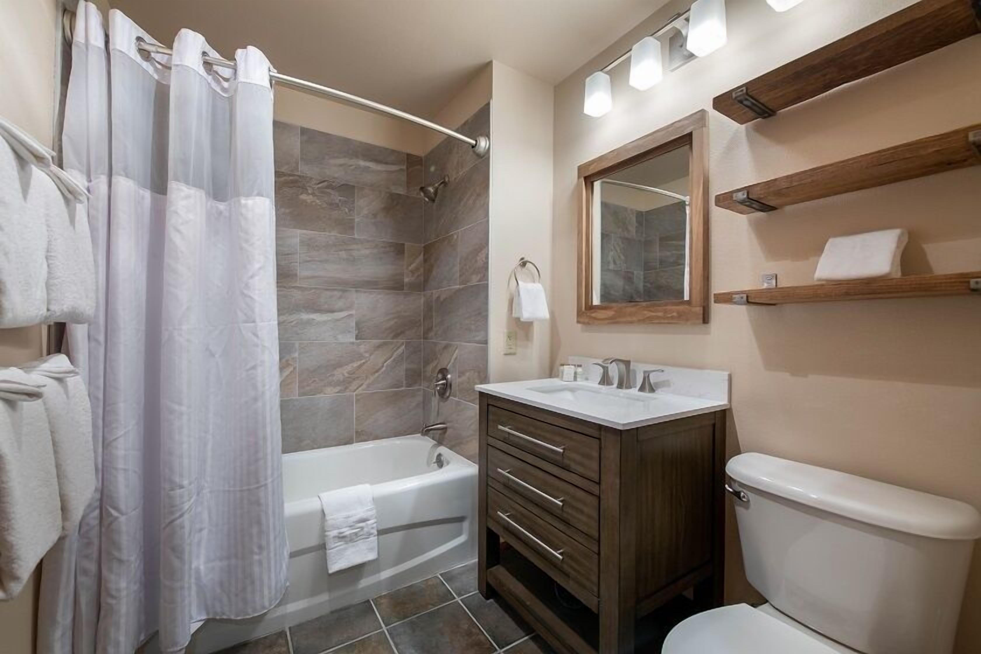 A bathroom with a bathtub, a toilet, a vanity with drawers, a mirror, and a shower curtain.