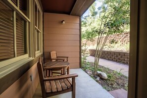 A wooden bench and table on a covered patio with a view of a brick wall and greenery. - Zephyr Mountain Lodge Condos (Winter Park)
