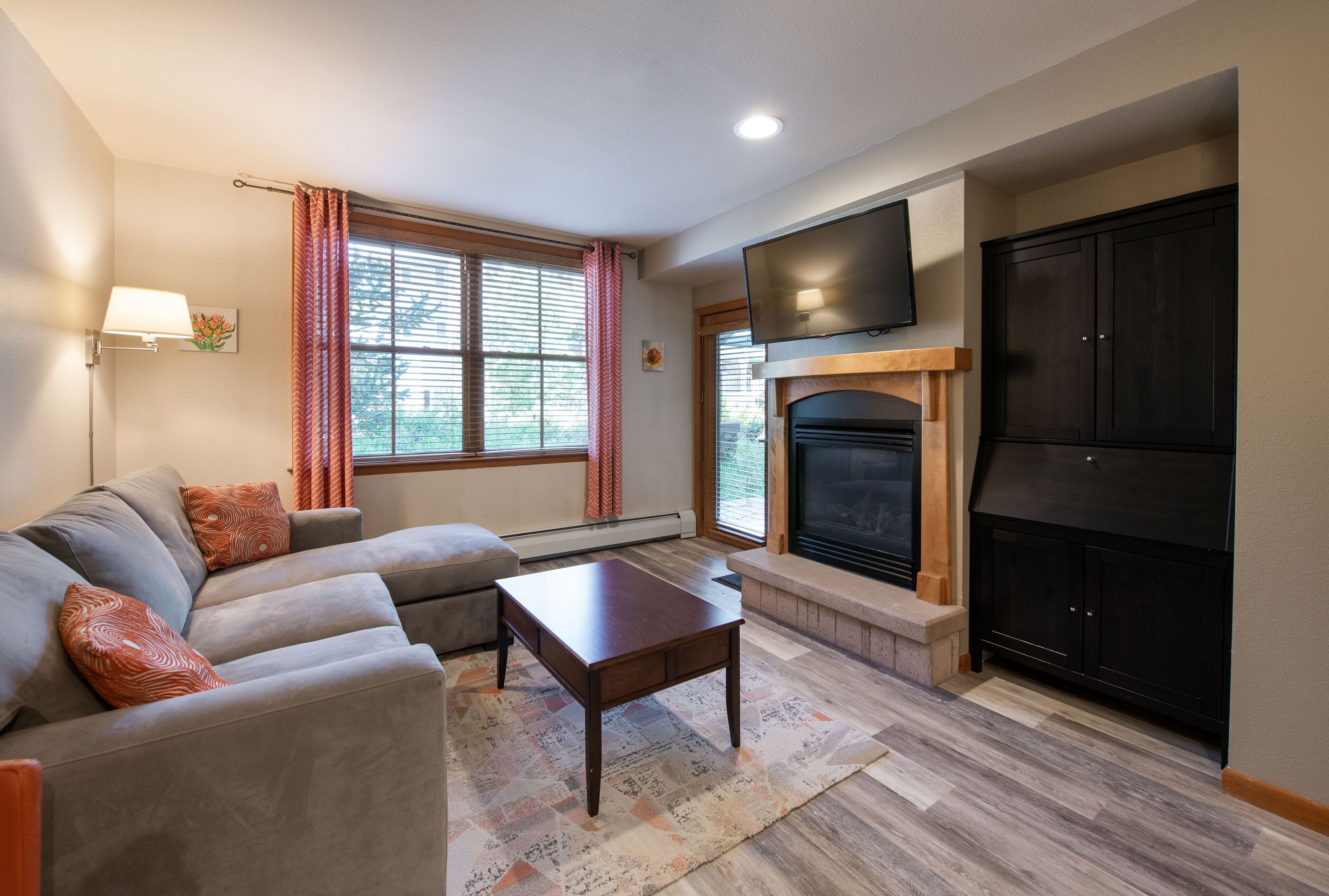 A living room with a sofa, a coffee table, a fireplace, and a TV mounted on the wall.