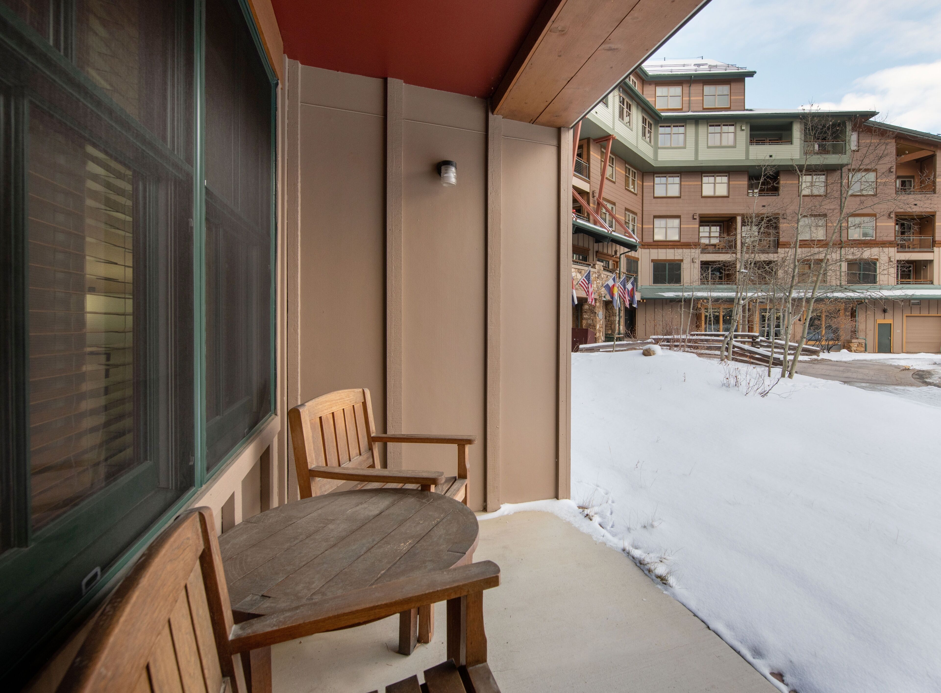 A balcony with wooden chairs, a window, and a view of a multi-story building with flags.