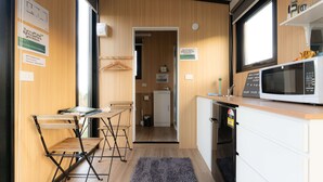 Een praktische keuken met een magnetron, spoelbak en een kleine koelkast. Er staat een houten tafel met stoelen en een vloerkleed.