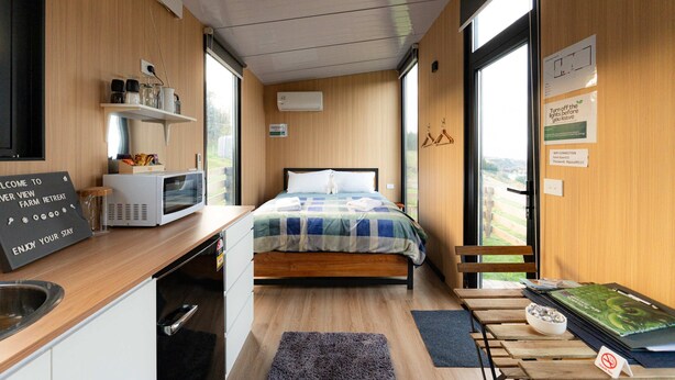Een kleine kamer met een bed, een magnetron, een klein wastafeltje en een raam met uitzicht.