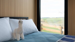 Een bed met een witte pluchen lama, witte kussens en een blauwe deken.