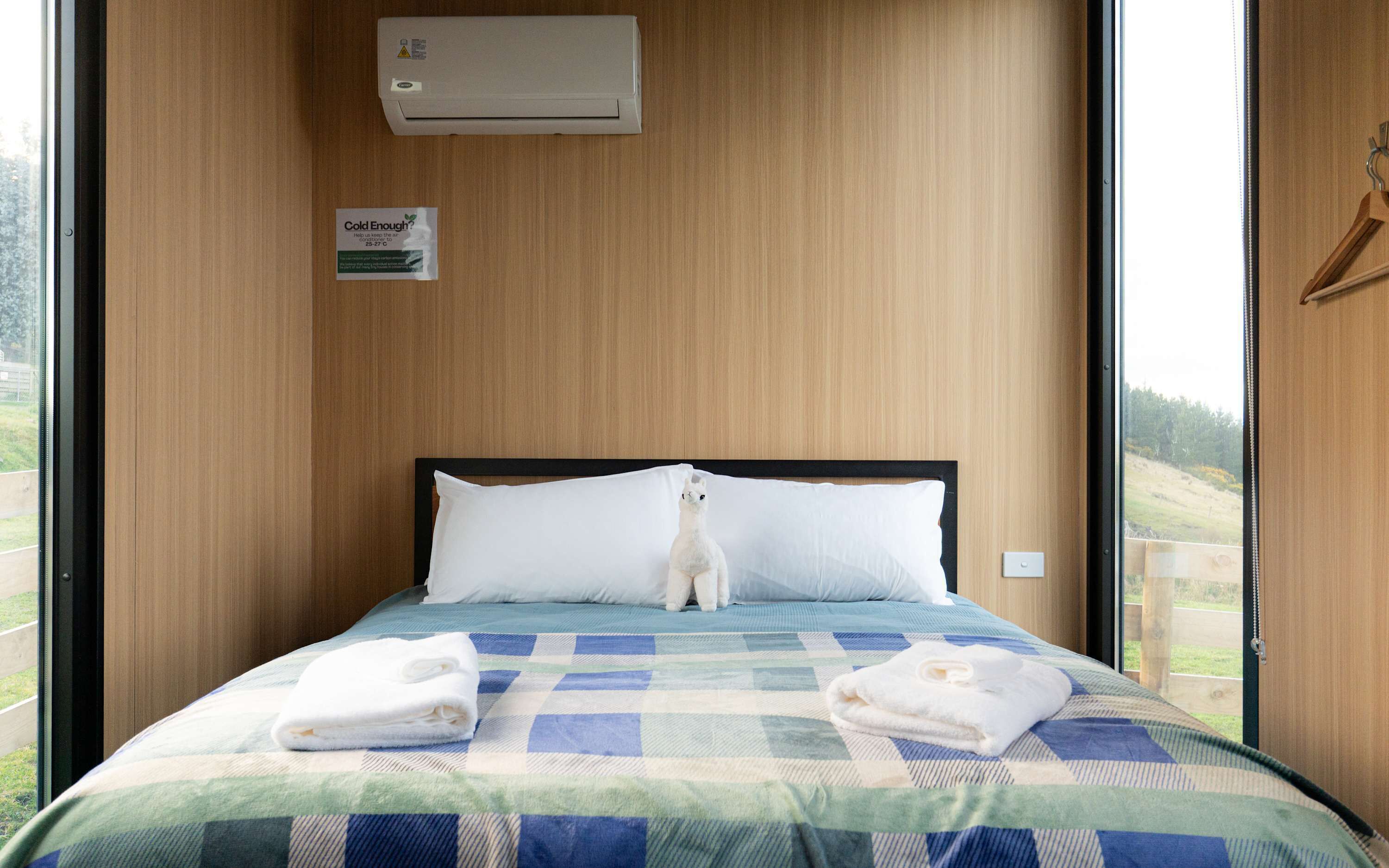 Una camera d'albergo con un letto, un condizionatore d'aria a parete, un cartello che indica la temperatura ambiente e vista all'esterno.