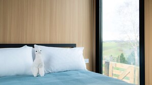 Ein Bett mit weißen Kissen und einem Stofftier in einem Zimmer mit Holzwandverkleidung und einem großen Fenster.