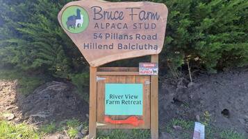 Placa de madeira para Bruce Farm Alpaca Stud na estrada Pillans, número 54, Hillend Balclutha, anunciando um refúgio rural com vista para o rio.