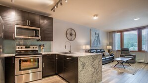 A modern kitchen with stainless steel appliances, a granite countertop island, and a dining area with a sofa and table.