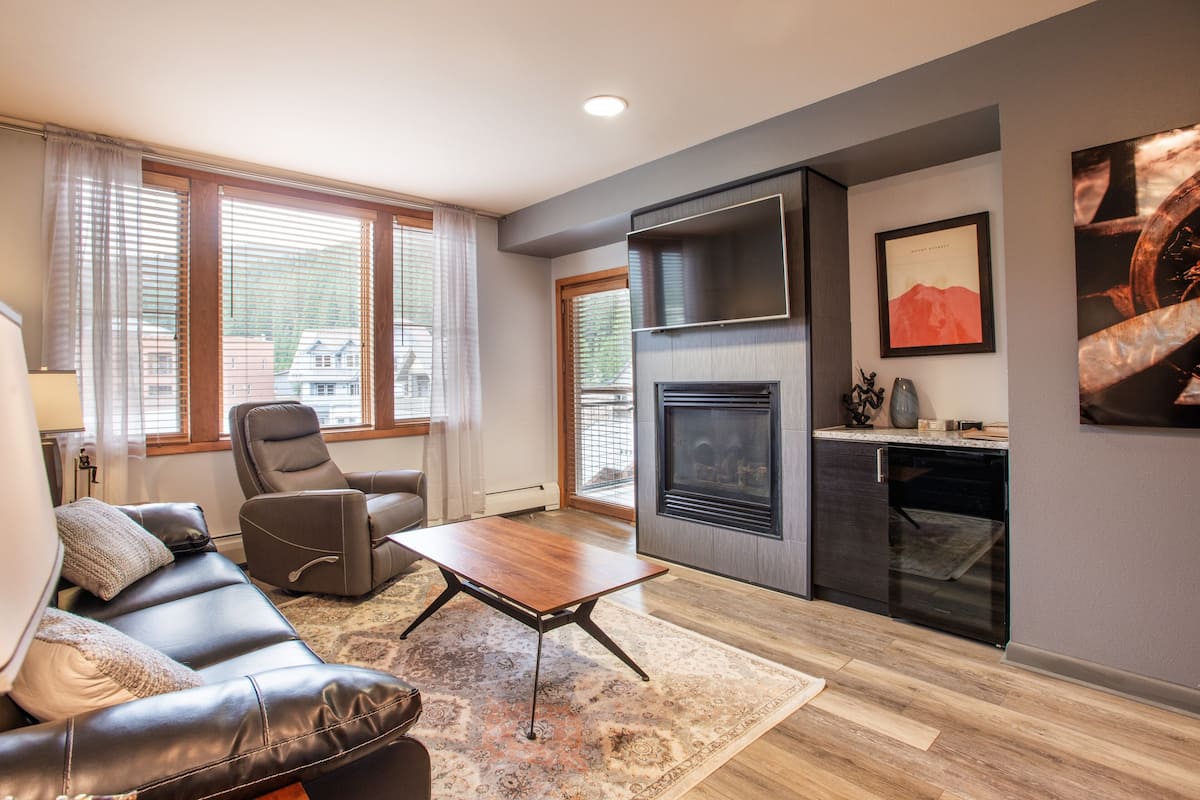 A modern living room with a leather sofa, a recliner, a wooden coffee table, and a fireplace.