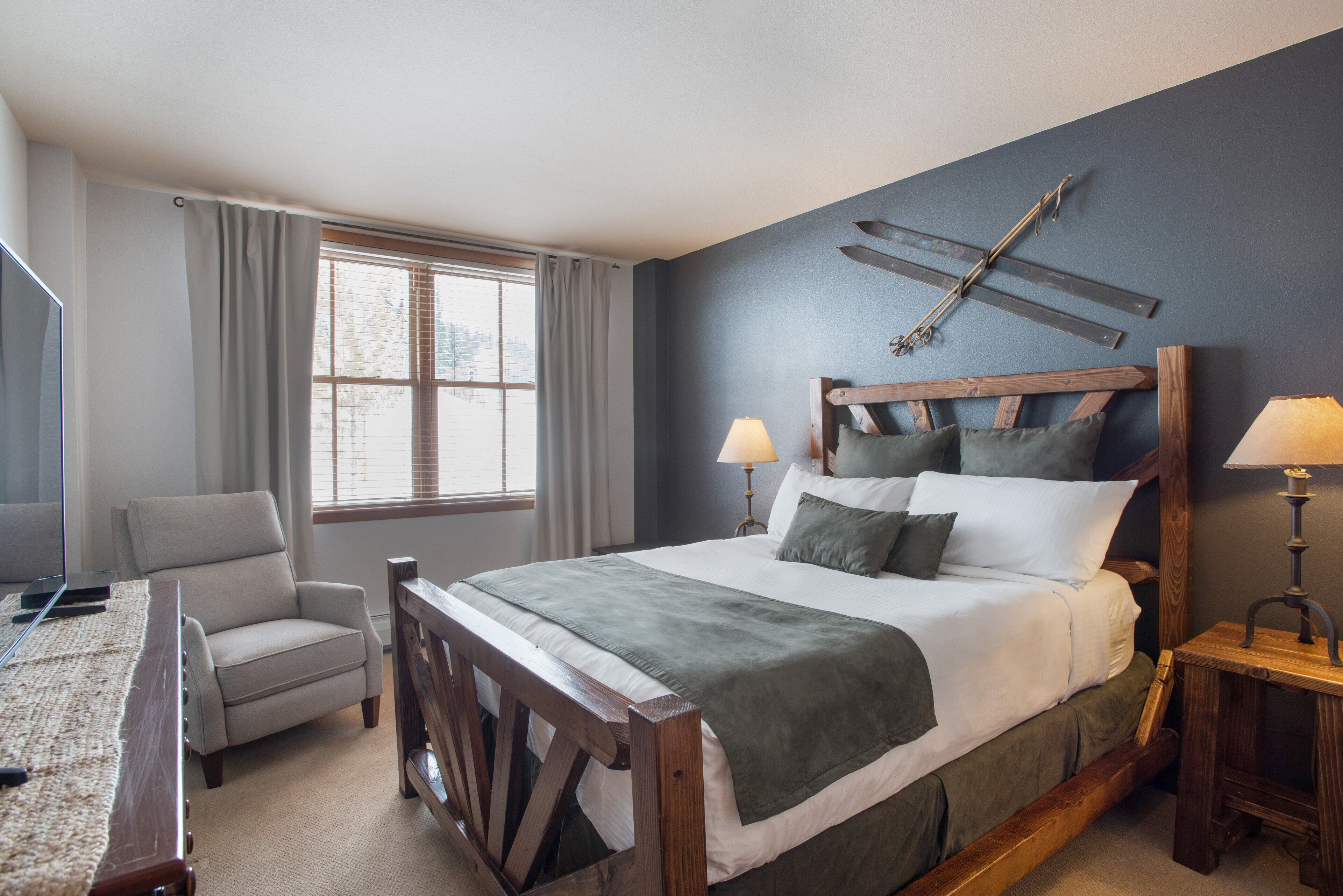A bedroom with a large bed, a chair, a desk, and a window with curtains.