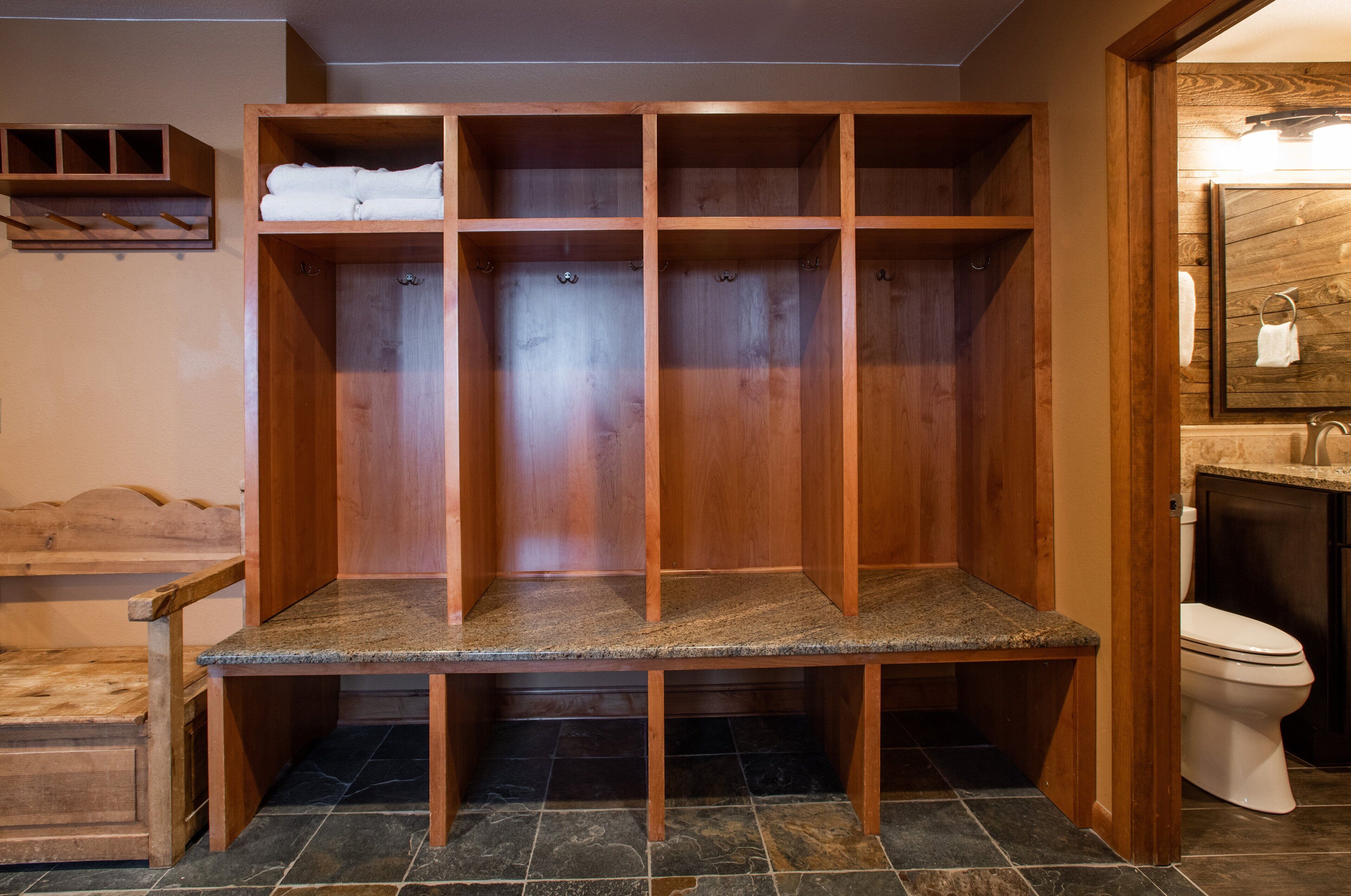 A wooden walk-in closet with shelves and a bench, a stone-tiled floor, and a bathroom with a toilet and sink.