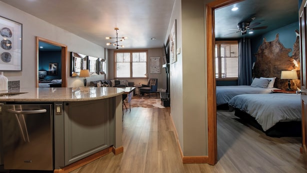 A modern kitchen with a dishwasher, a dining area with a table and chairs, a living room with a sofa and a coffee table, and a bedroom with a bed and a ceiling fan.