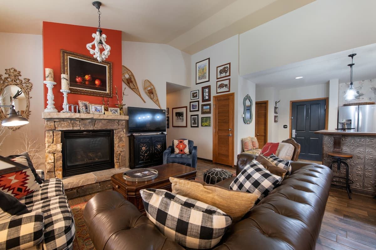 Una sala de estar con chimenea, televisor, sofá con cojines cuadriculados y un comedor con barra.