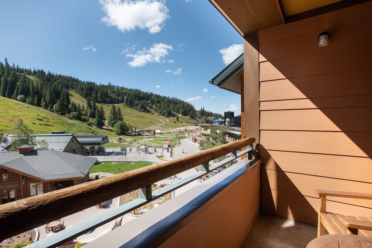 Un balcón con vistas a un paisaje montañoso, un edificio con techo inclinado y barandilla de madera.