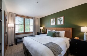 A neatly arranged hotel room with a large bed, two bedside tables with lamps, a bench, and a window with curtains. - Winter Park CO Condos - Zephyr Mountain Lodge (Winter Park)