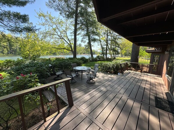 A wooden deck with a table and chairs, surrounded by greenery and a view of a lake.