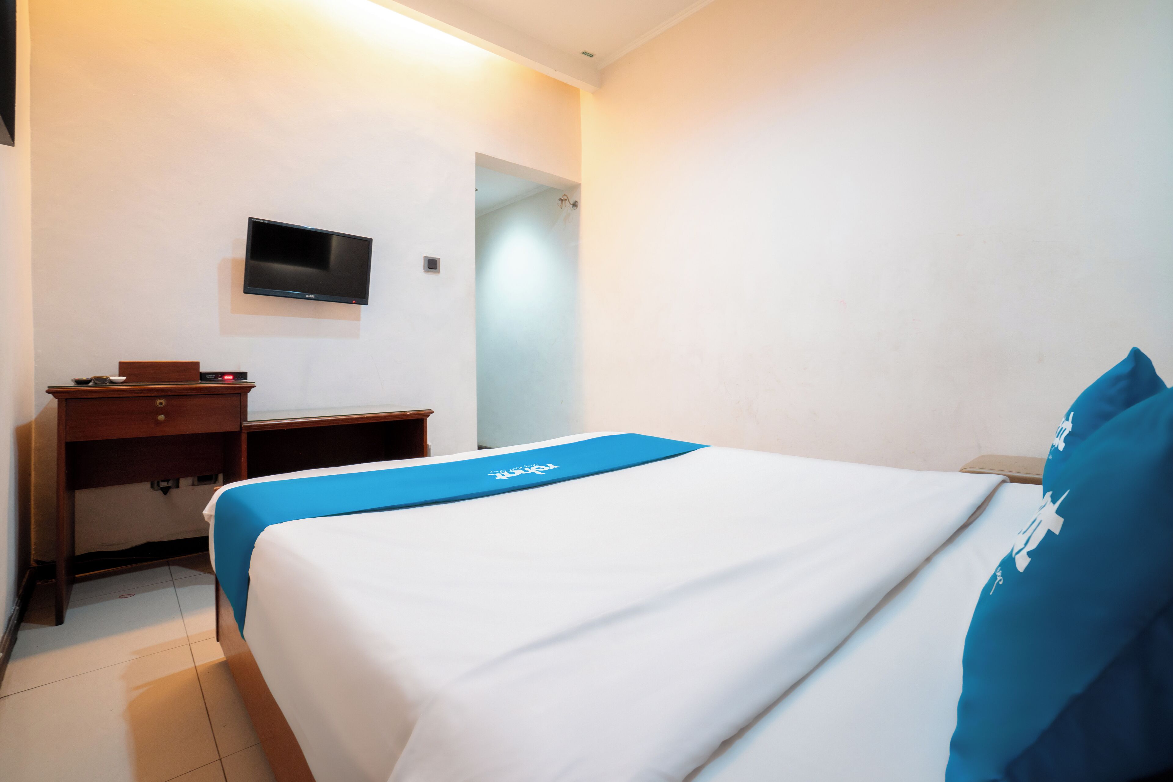 Una habitación de hotel con una cama, un escritorio y un televisor montado en la pared.