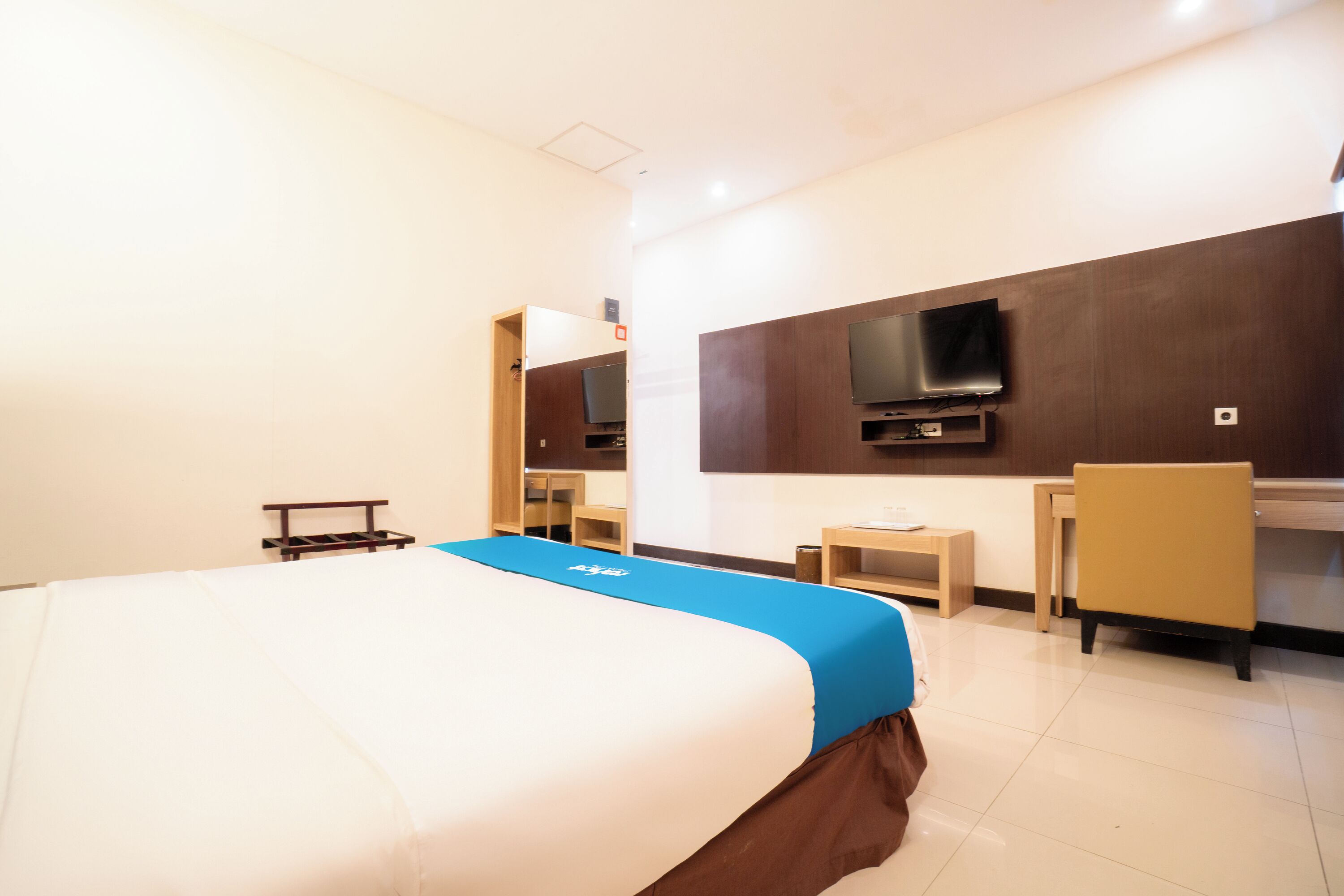 Ein Hotelzimmer mit einem großen Bett, einem Schreibtisch, einem Sessel, einem an der Wand befestigten Fernseher und einem kleinen Tisch.