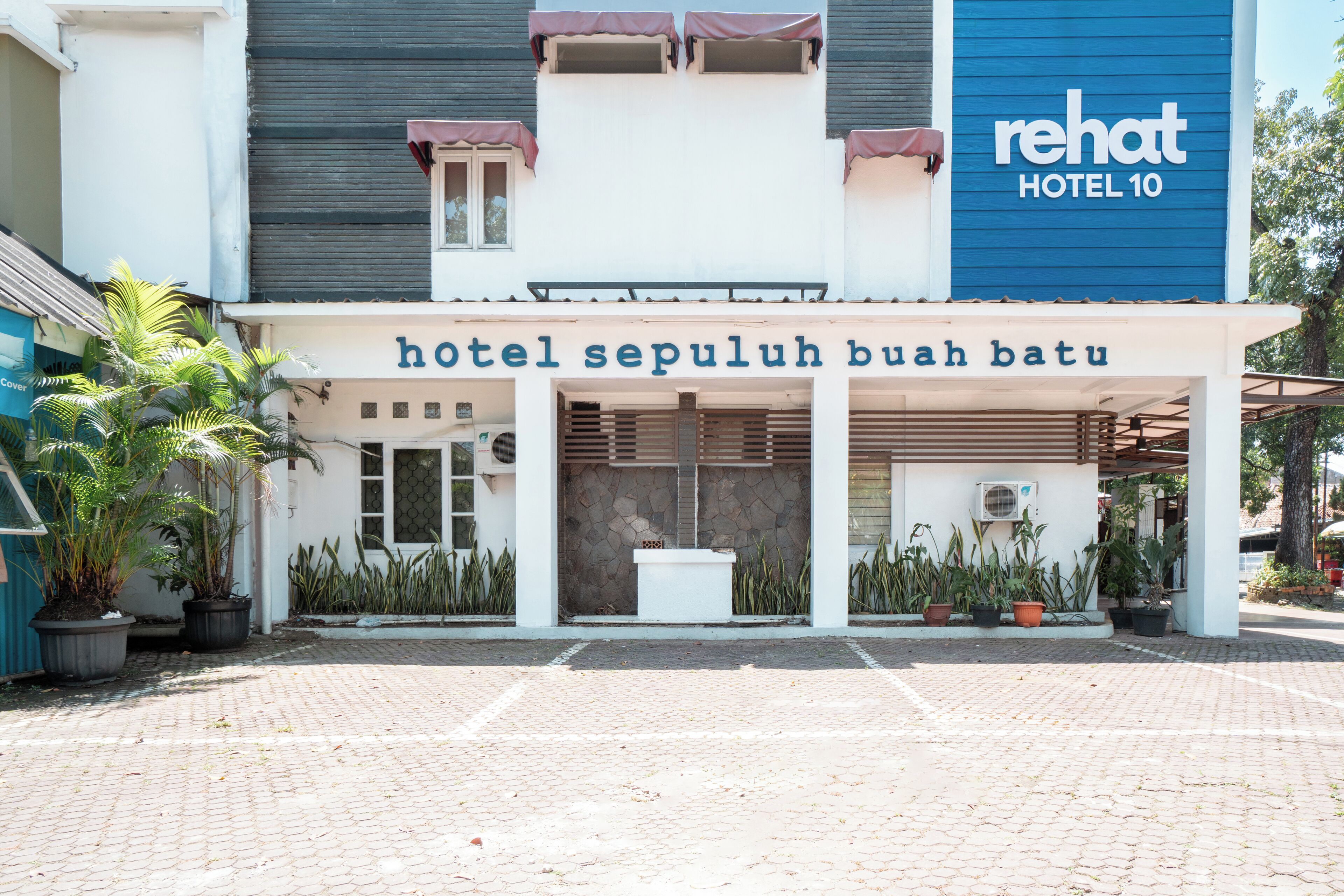 Ein Hotel Eingang mit einem Schild, auf dem 'hotel sepuluh buah batau' steht, und einem großen Schild mit der Aufschrift 'rehat hotel 10' am Gebäude.