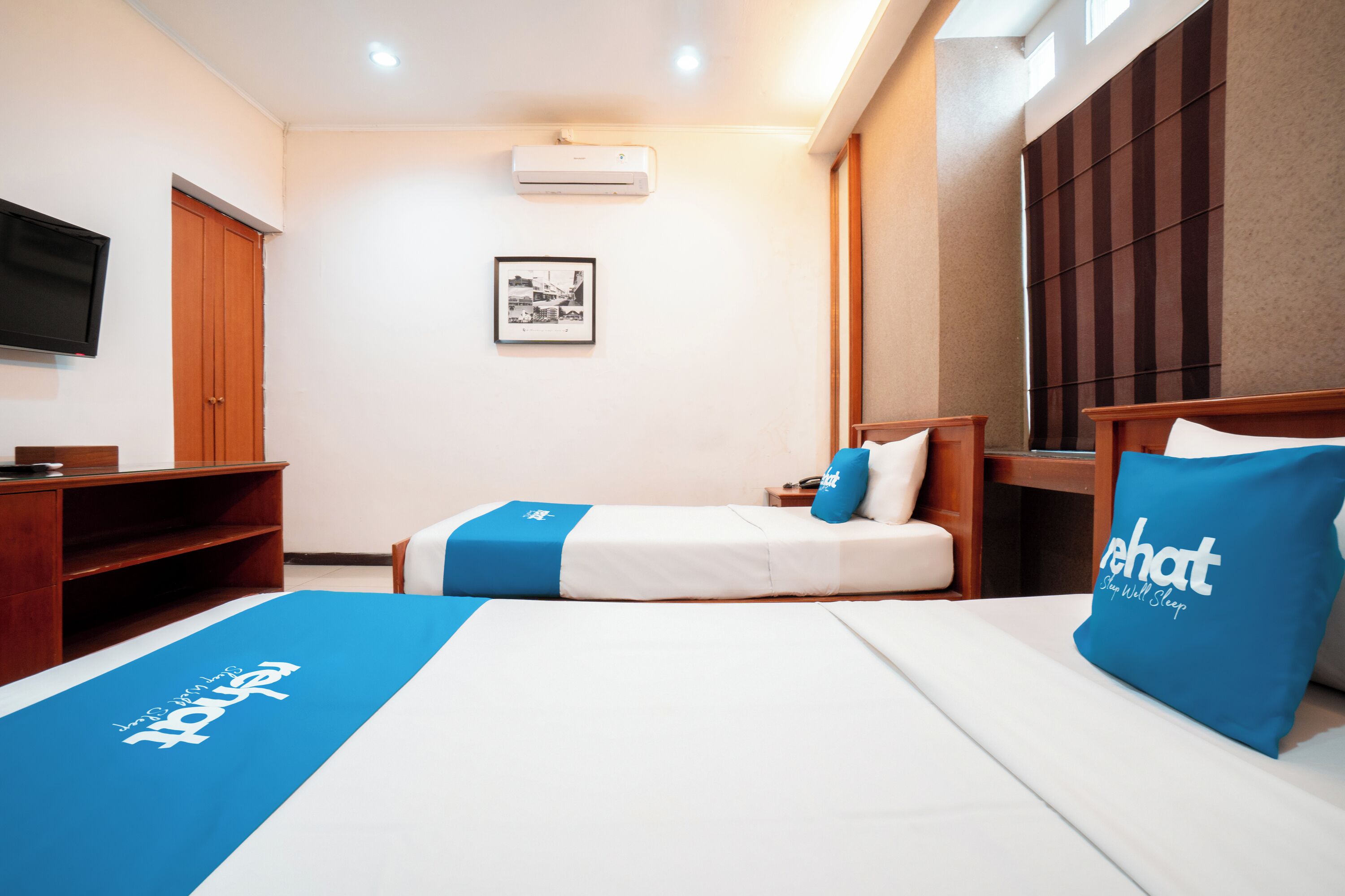 A hotel room with two beds, a TV, a wardrobe, and a framed picture on the wall.