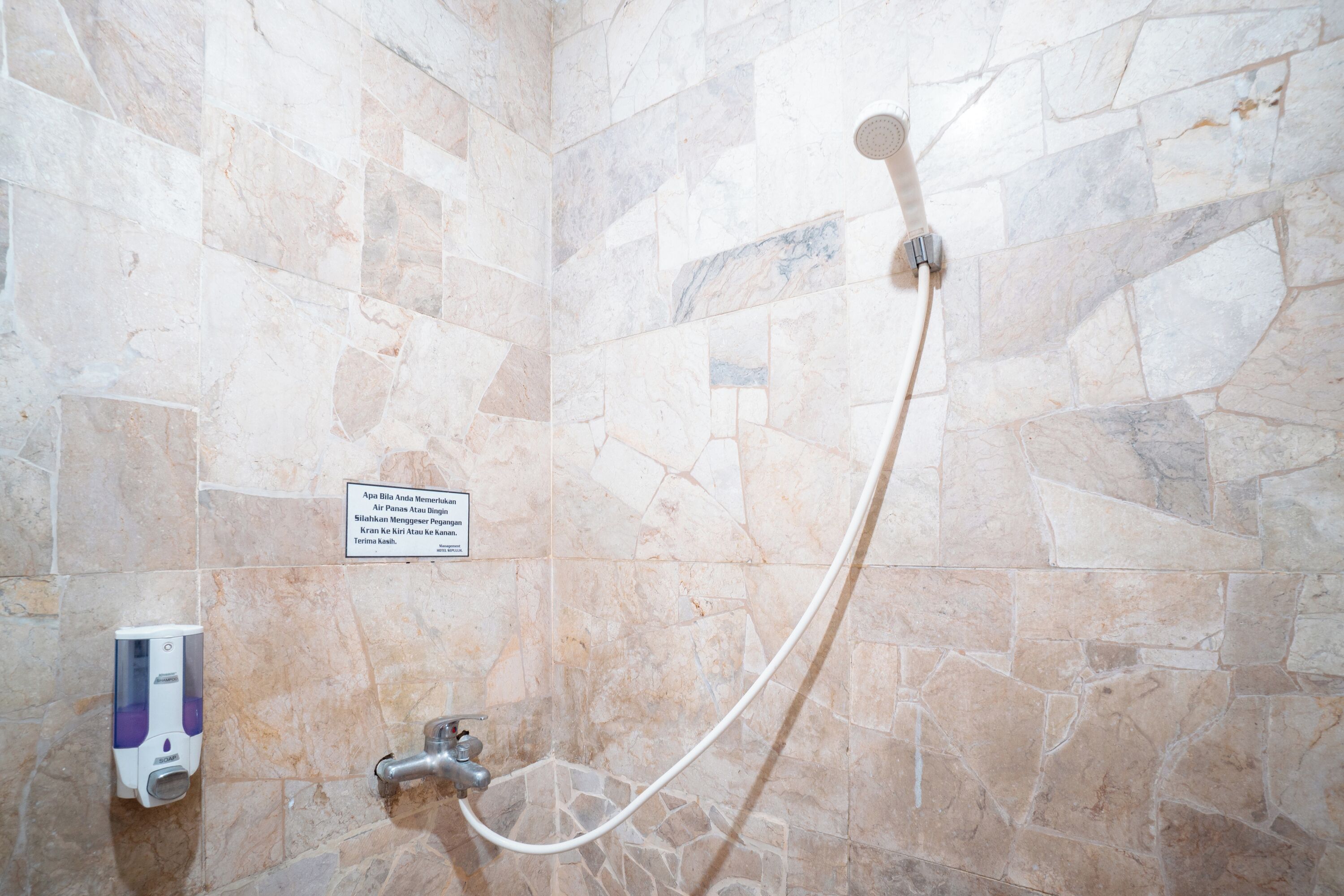 A shower area with stone tiles, a handheld showerhead, a soap dispenser, and a sign with text.