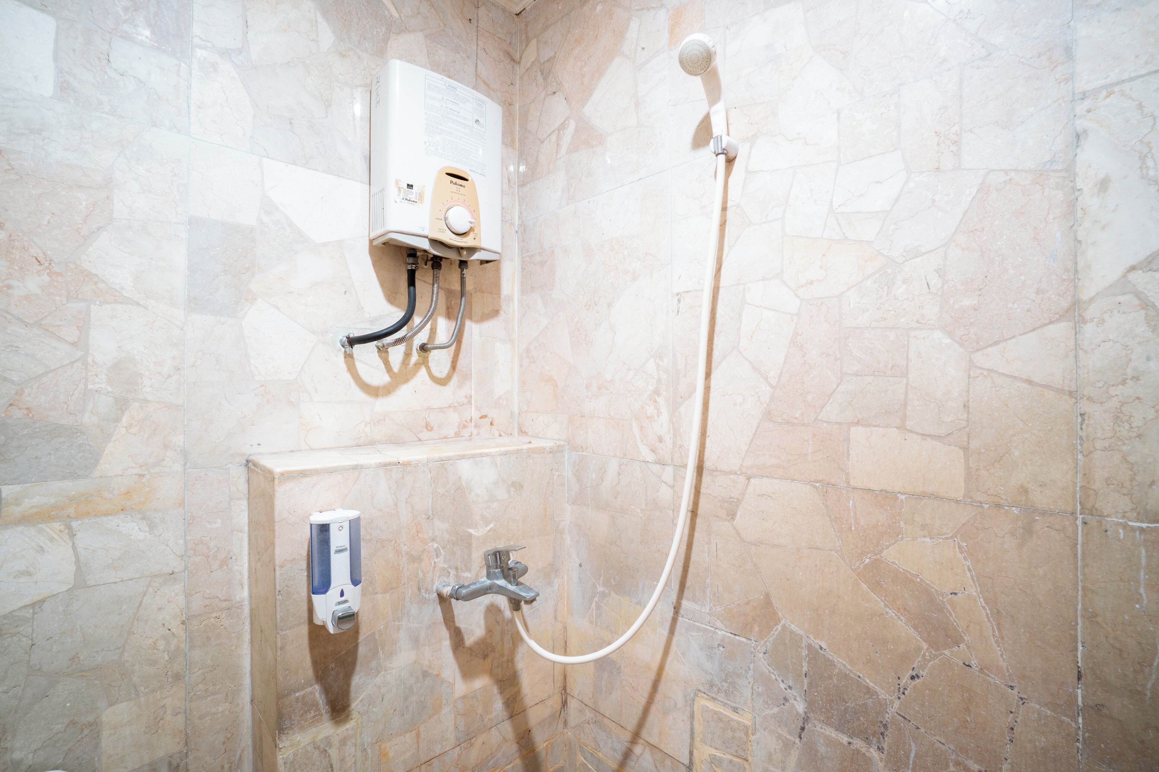 A bathroom with a shower, a soap dispenser, and a water heater.
