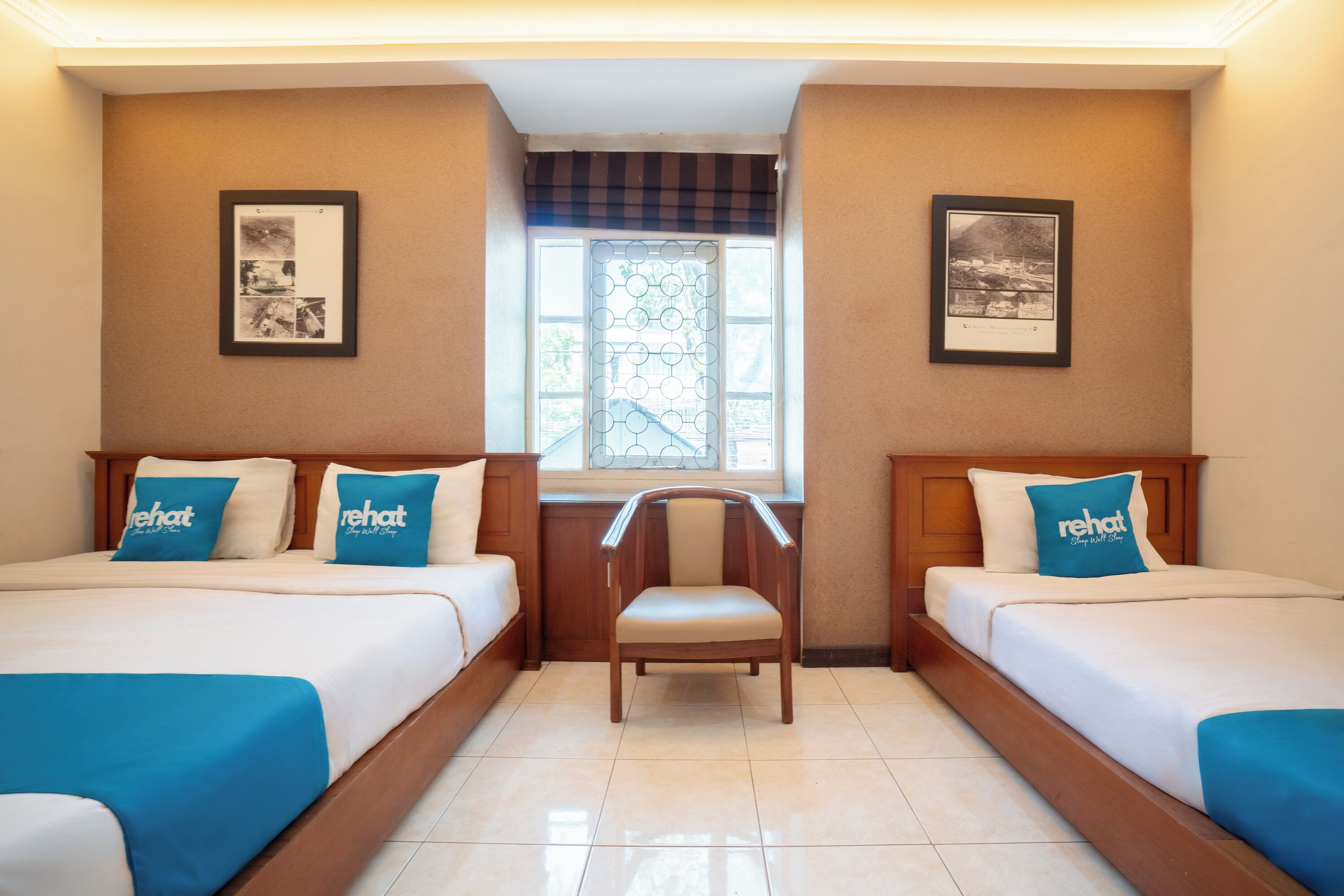 A hotel room with two beds, a chair, and two framed pictures on the walls.