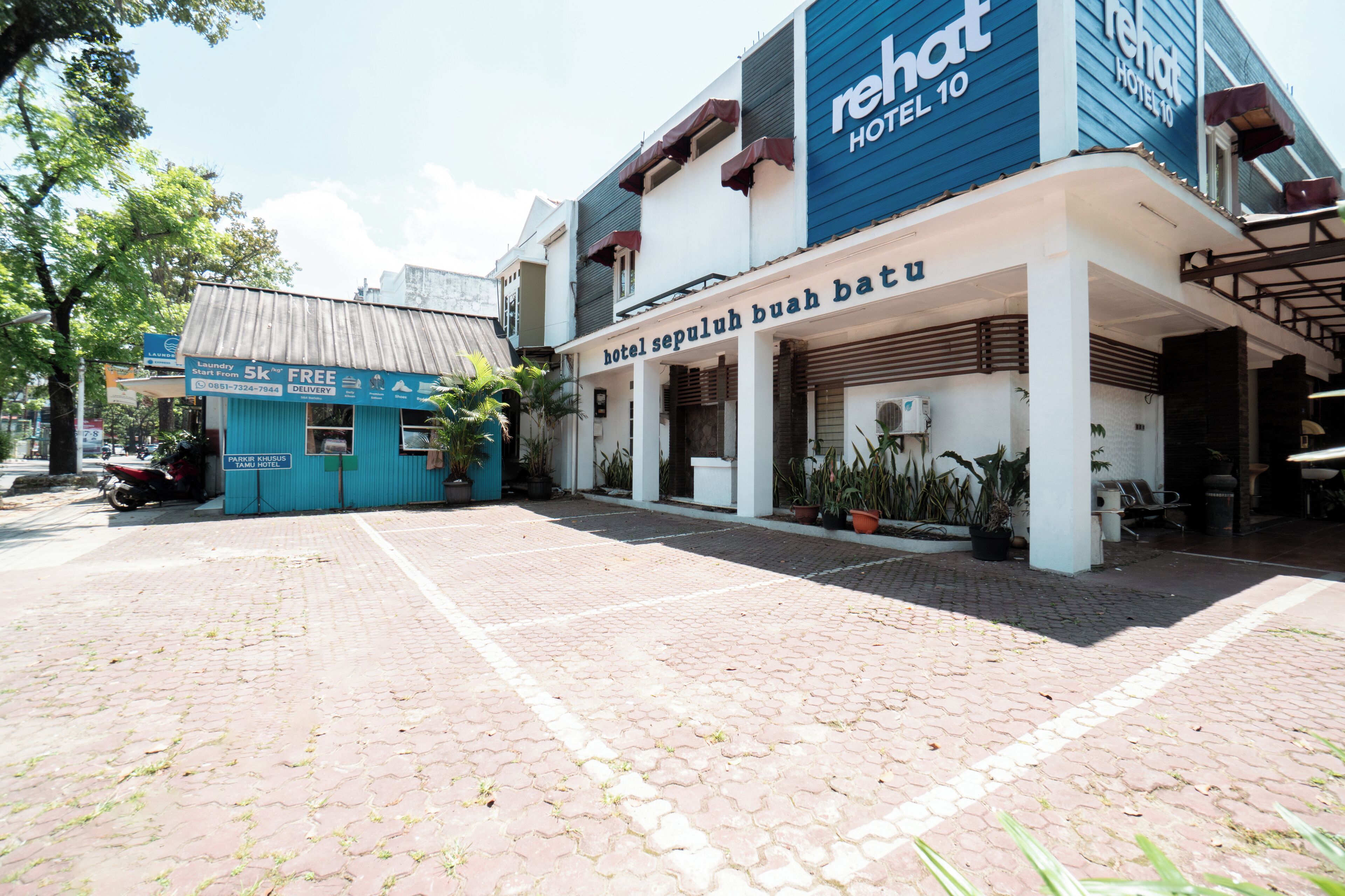 A hotel with a blue and white facade, a covered entrance, and a paved courtyard.