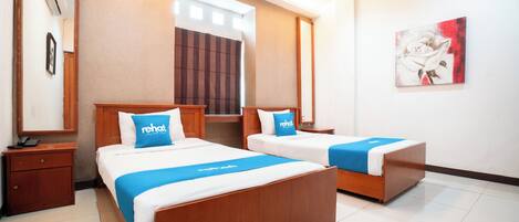 A hotel room with two beds, a wooden headboard, a blue bed runner, a nightstand, a phone, and a painting on the wall.