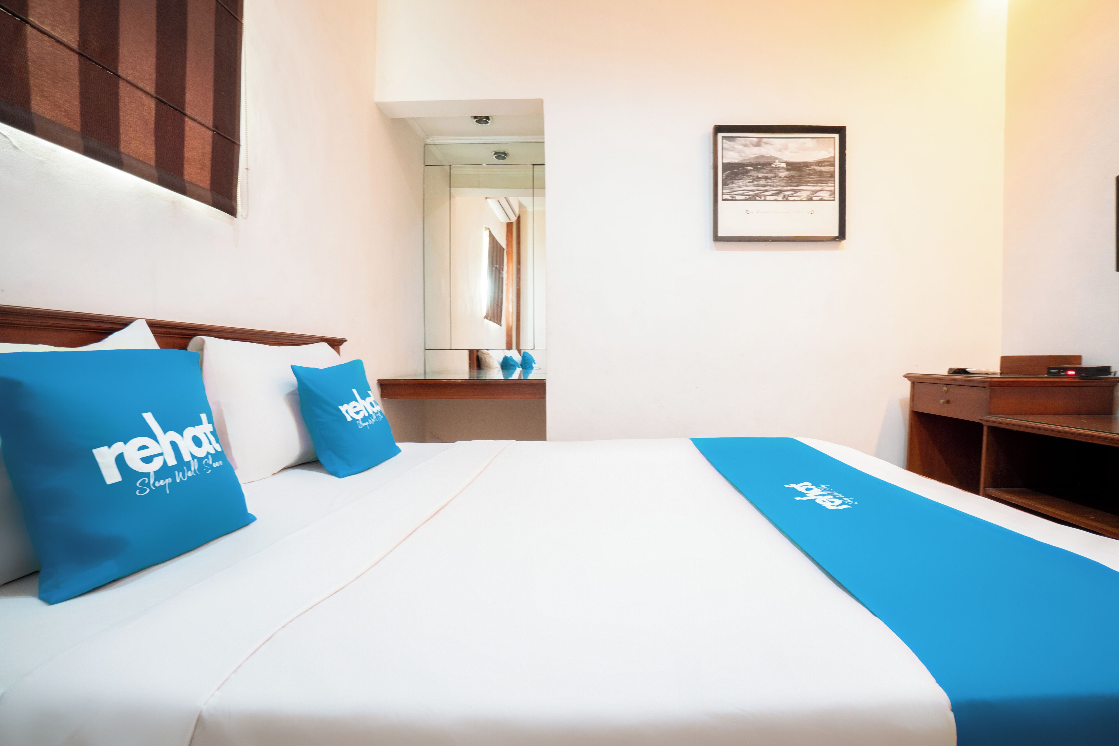 A hotel room with a bed, a nightstand, a mirror, and a framed picture on the wall.