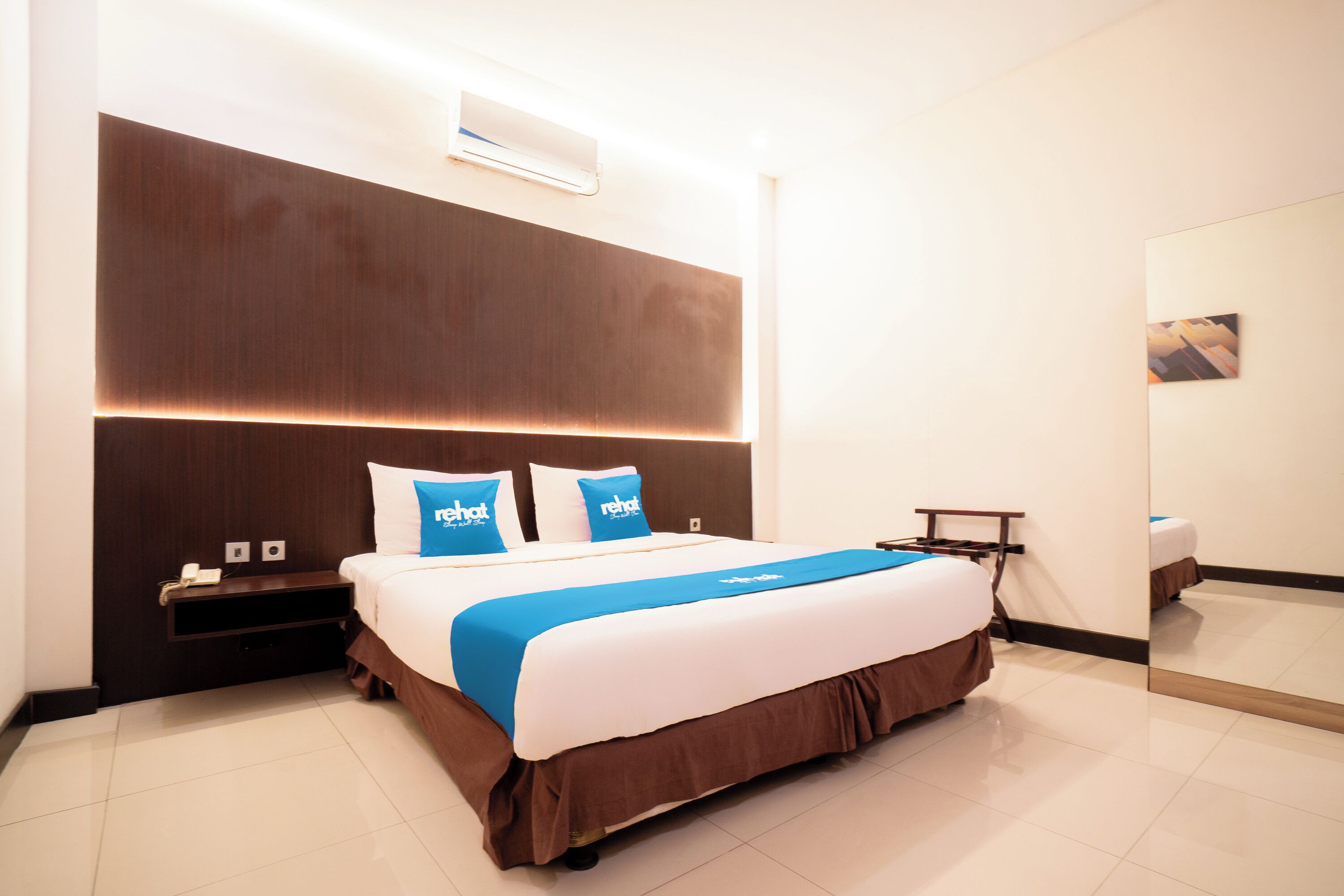 Une chambre d’hôtel moderne avec un grand lit, une table de chevet, une petite table et un climatiseur fixé au mur.