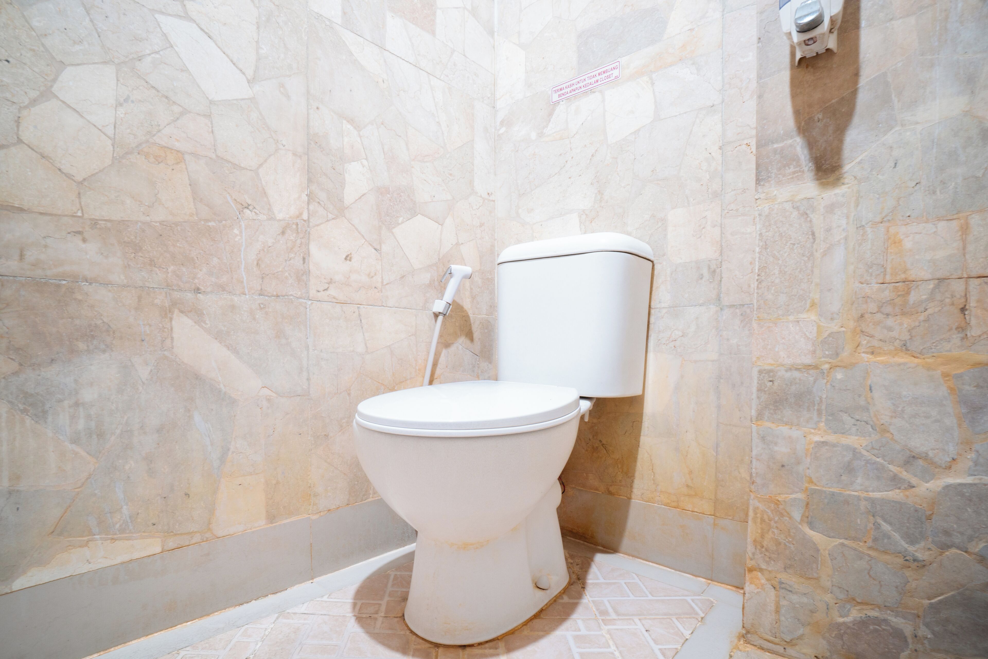 Un baño con inodoro blanco, paredes de piedra y suelo de baldosas.