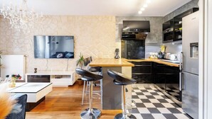 A modern kitchen with a central island, black bar stools, a chandelier, and a stone wall. - Escapade Exotique-Private Terrace-Love&Jacuzzi (Franconville)